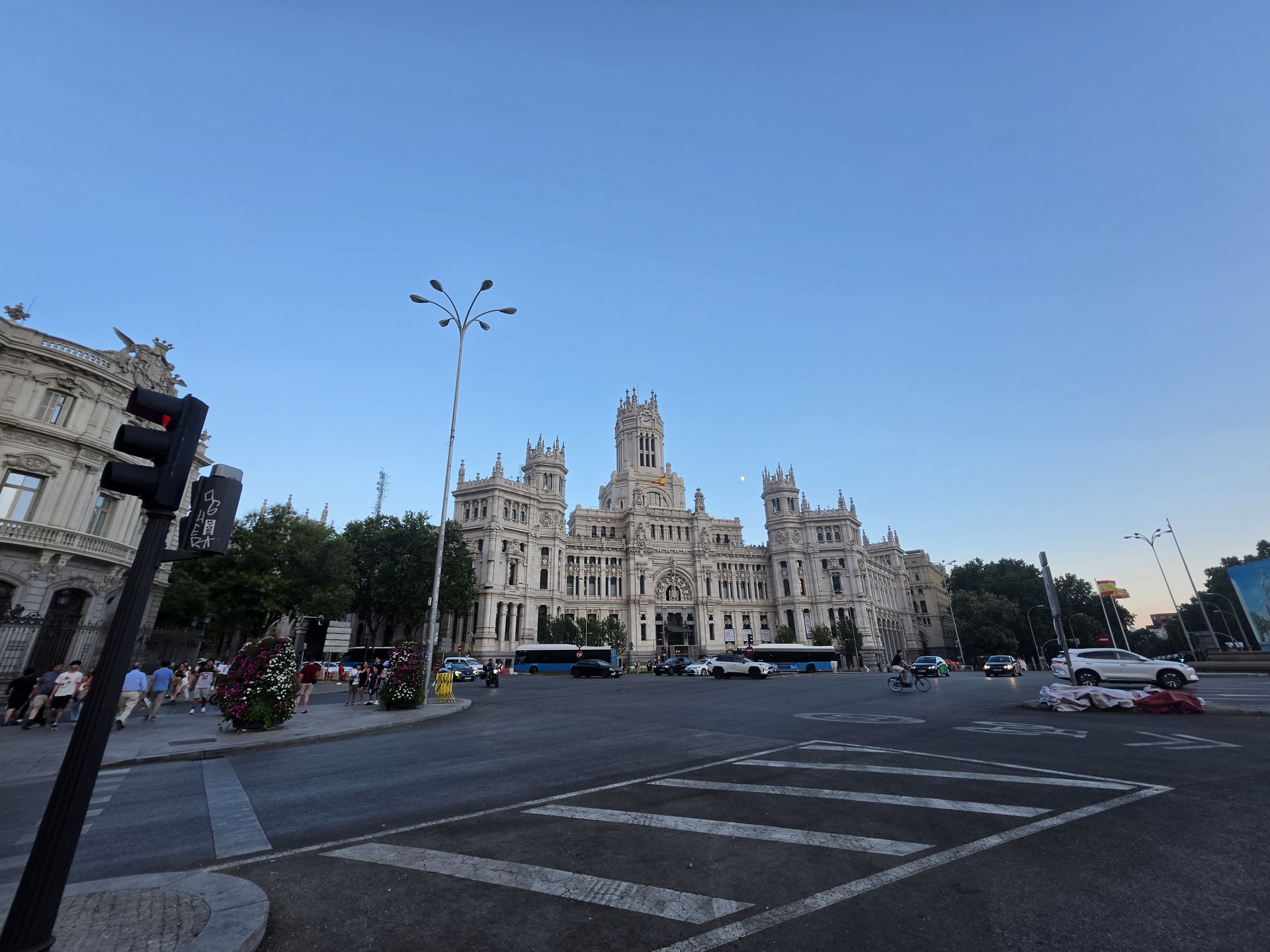 Palacio de Cibeles en Madrid al atardecer, rodeado de autos y peatones en una intersección concurrida.