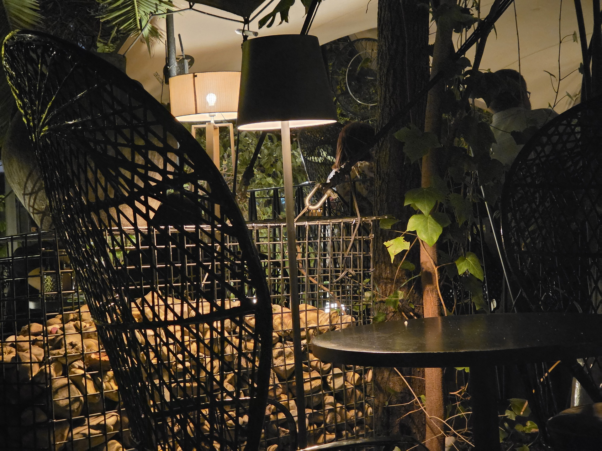 Terraza nocturna con sillones de mimbre, iluminación cálida y vegetación, creando ambiente acogedor y natural.