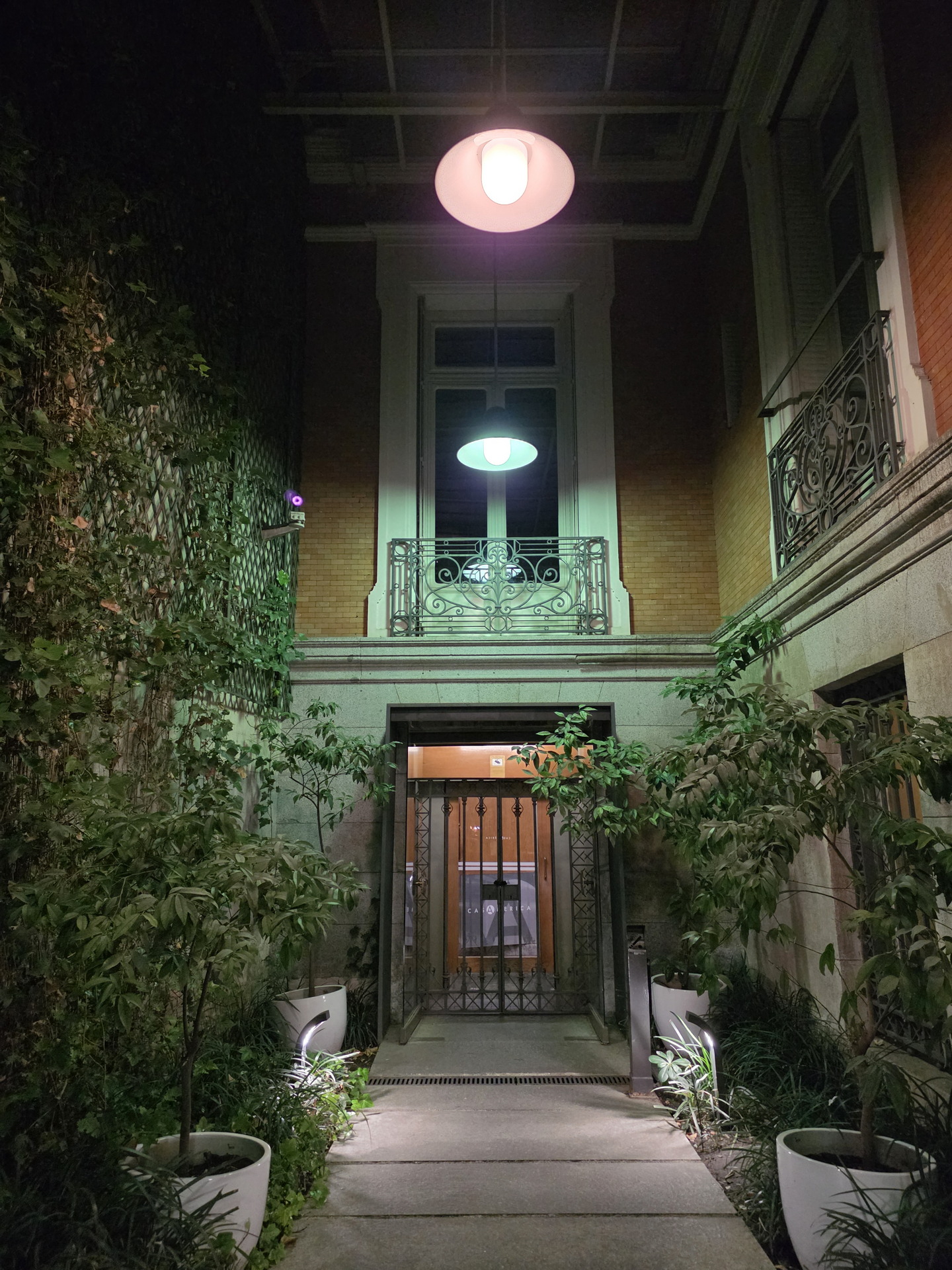 Entrada iluminada con plantas y faroles en un edificio de noche.