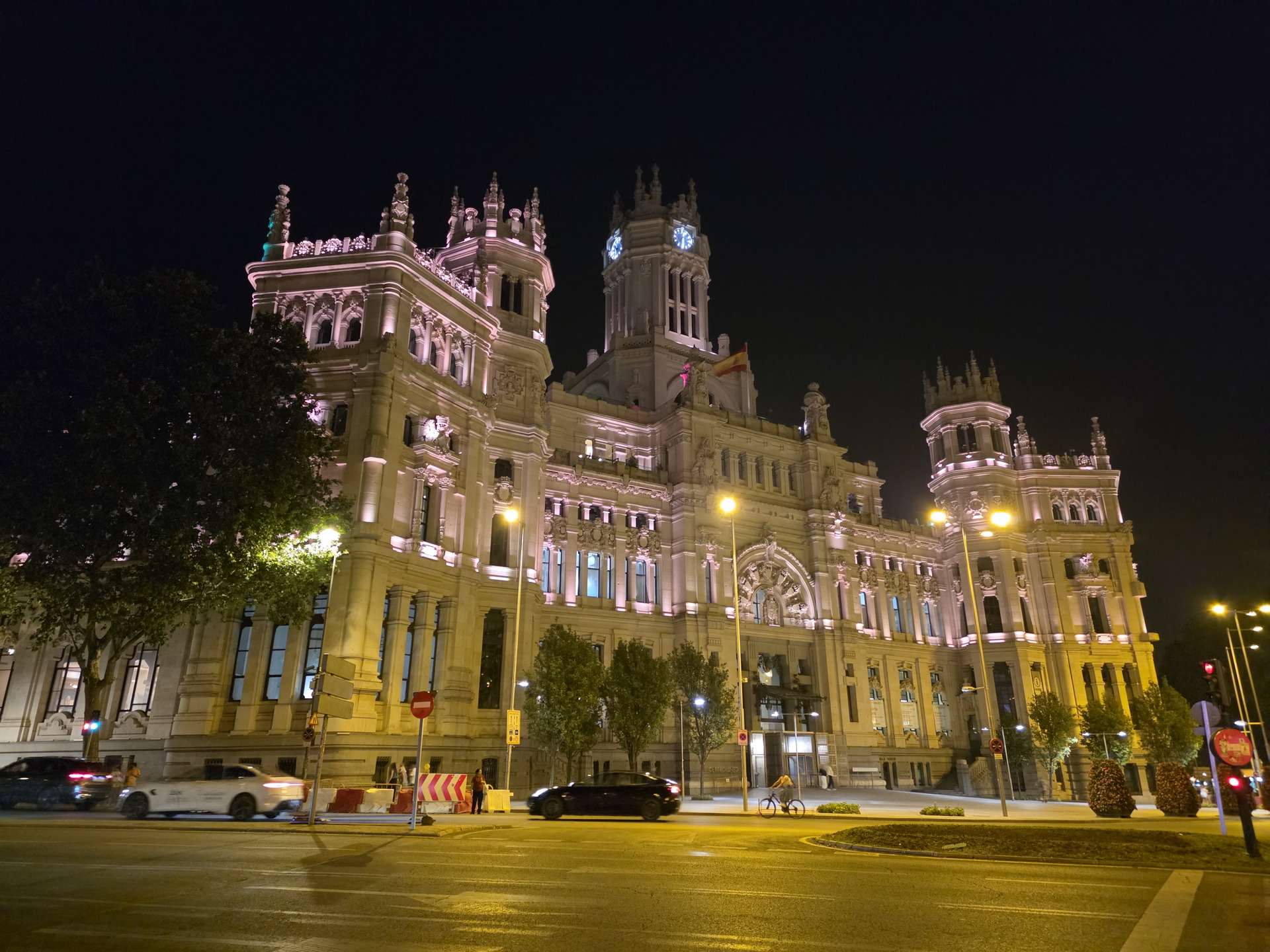 Edificio de Correos en Madrid iluminado por la noche, con luces amarillas y tráfico en movimiento.