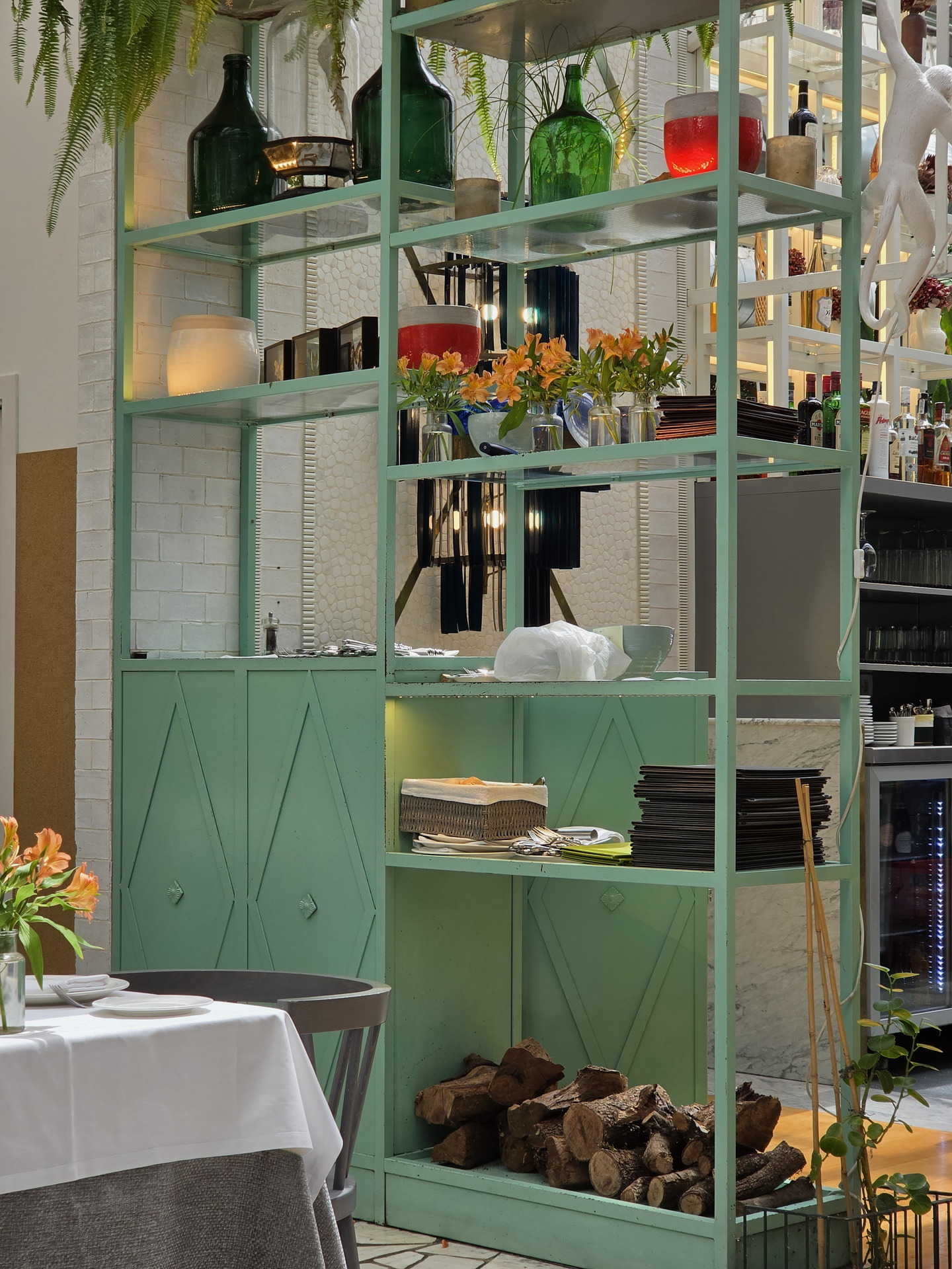 Estantería de restaurante con decoración verde, flores naranjas y botellas. Ambiente acogedor y moderno.