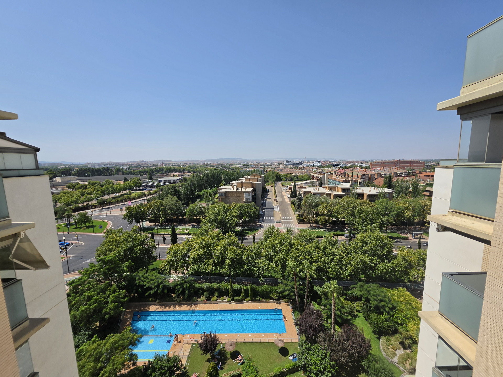 Vista aérea de una piscina rodeada de árboles y edificios residenciales bajo un cielo despejado.