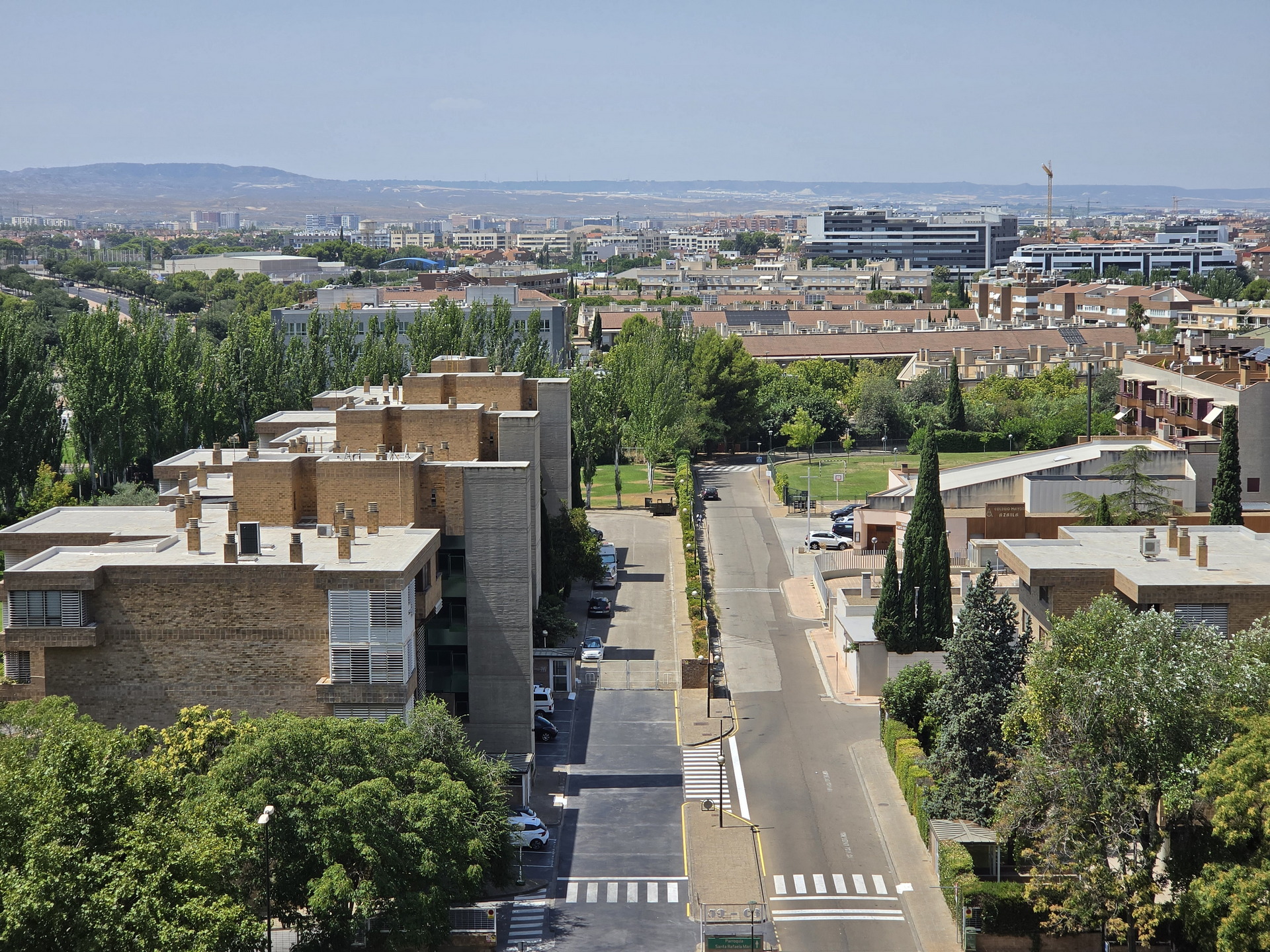 Vista panorámica de un barrio residencial con edificios de ladrillo, calles arboladas y fondo montañoso.