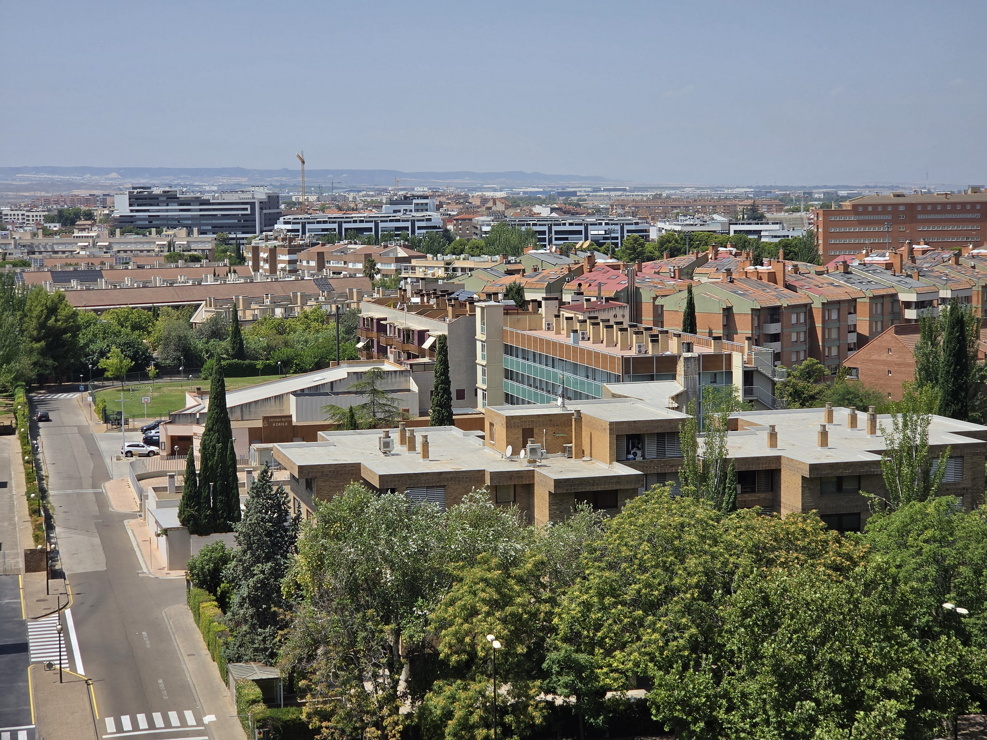 Vista panorámica de zona urbana con edificios residenciales rodeados de árboles bajo un cielo despejado.