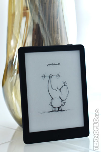 E-reader con pantalla encendida, mostrando dibujo de un elefante levantando pesas. Fondo con jarrón dorado.