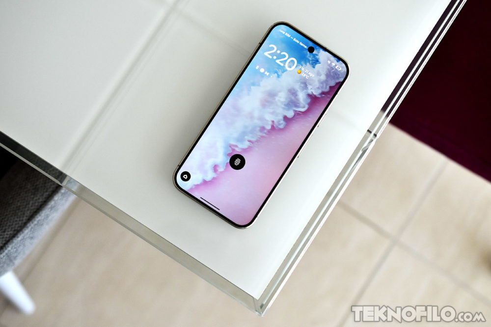 Smartphone sobre mesa de cristal con pantalla encendida mostrando hora y clima, diseño moderno y elegante.