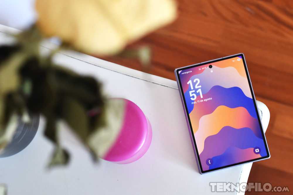 El Galaxy Z Fold8 dispara sus ventas un 65% en España y conquista a usuarios de otras marcas Teléfono inteligente sobre mesa blanca, pantalla colorida mostrando hora y fecha, junto a objeto y flor borrosos.