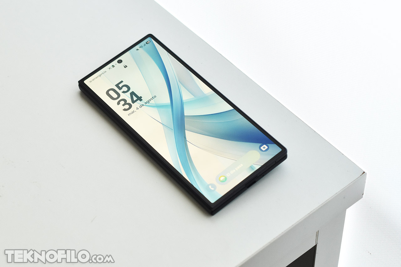 Smartphone moderno en una mesa blanca con pantalla encendida y diseño azul abstracto.
