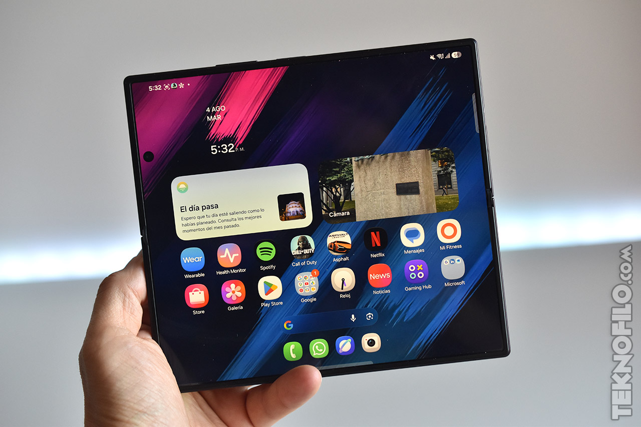 Pantalla de un dispositivo plegable con aplicaciones abiertas, mostrando la hora y notificaciones en fondo colorido.