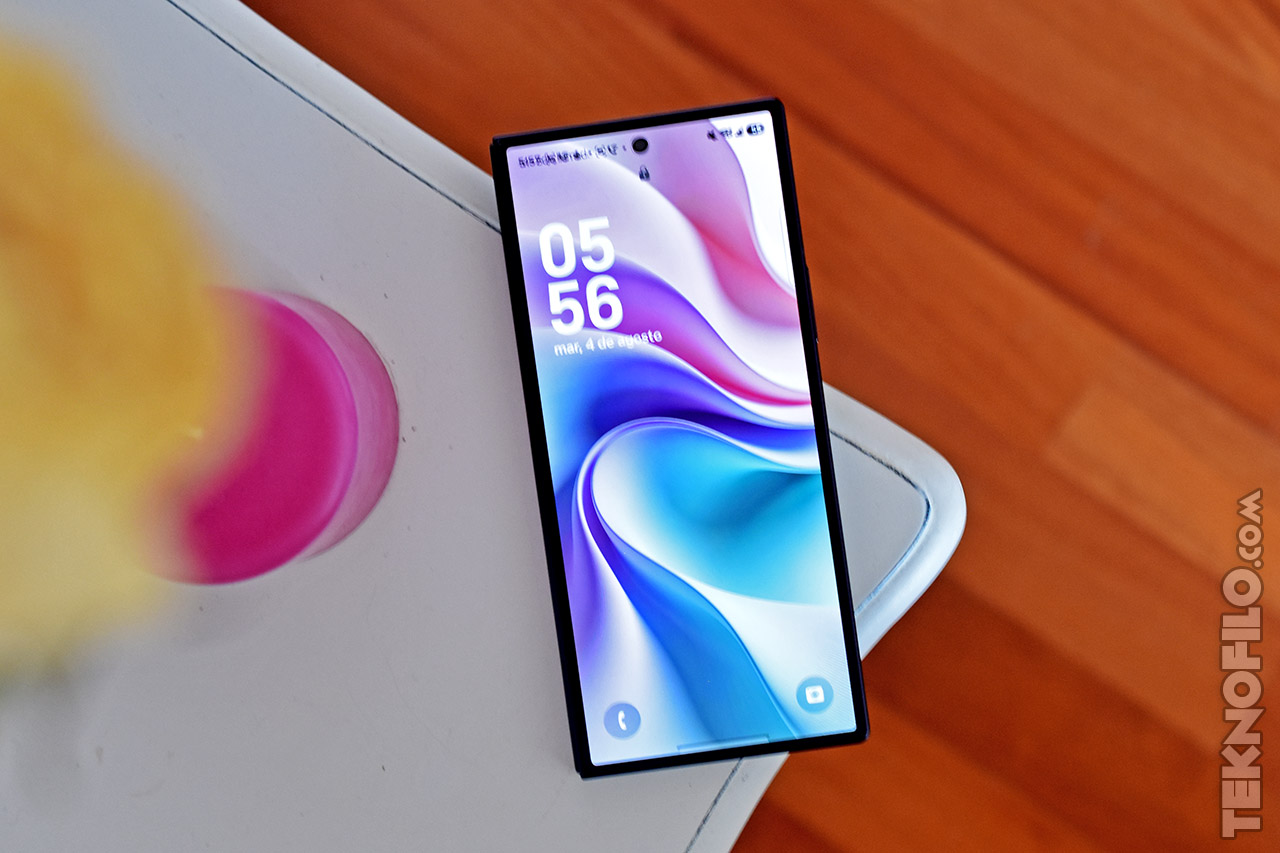 Teléfono inteligente moderno sobre mesa blanca, pantalla encendida con diseño colorido, hora 05:56 AM.