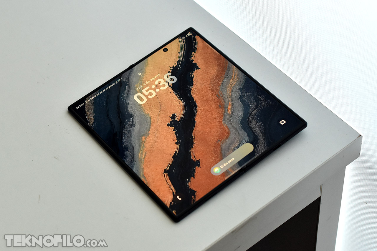 Pantalla de smartphone plegable con diseño artístico abstracto sobre una mesa blanca.