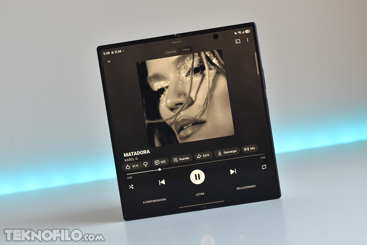 Pantalla de smartphone plegable mostrando la canción Matadora de Karol G en un entorno con fondo azul.
