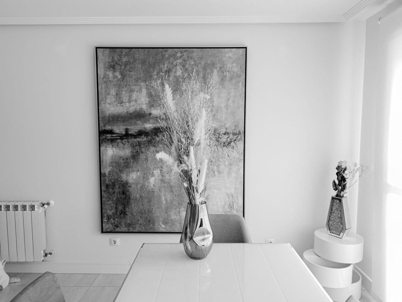 Comedor moderno en blanco y negro con pintura abstracta y jarrón. Decoración minimalista y elegante.