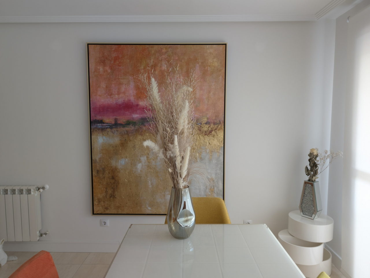 Pintura abstracta colorida en sala moderna con jarrón y mesa blanca. Decoración elegante y minimalista.