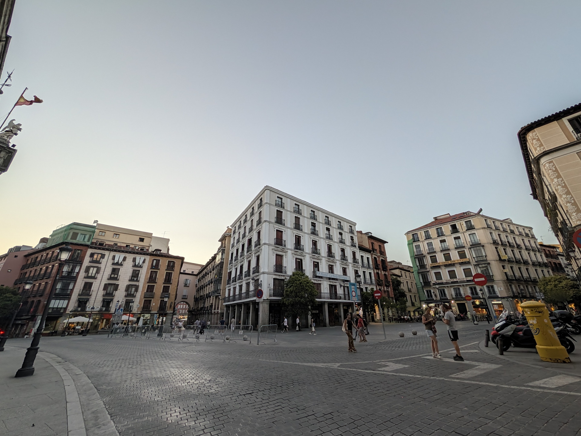 Vista de un cruce peatonal con edificios históricos y personas paseando al atardecer en una plaza de ciudad.