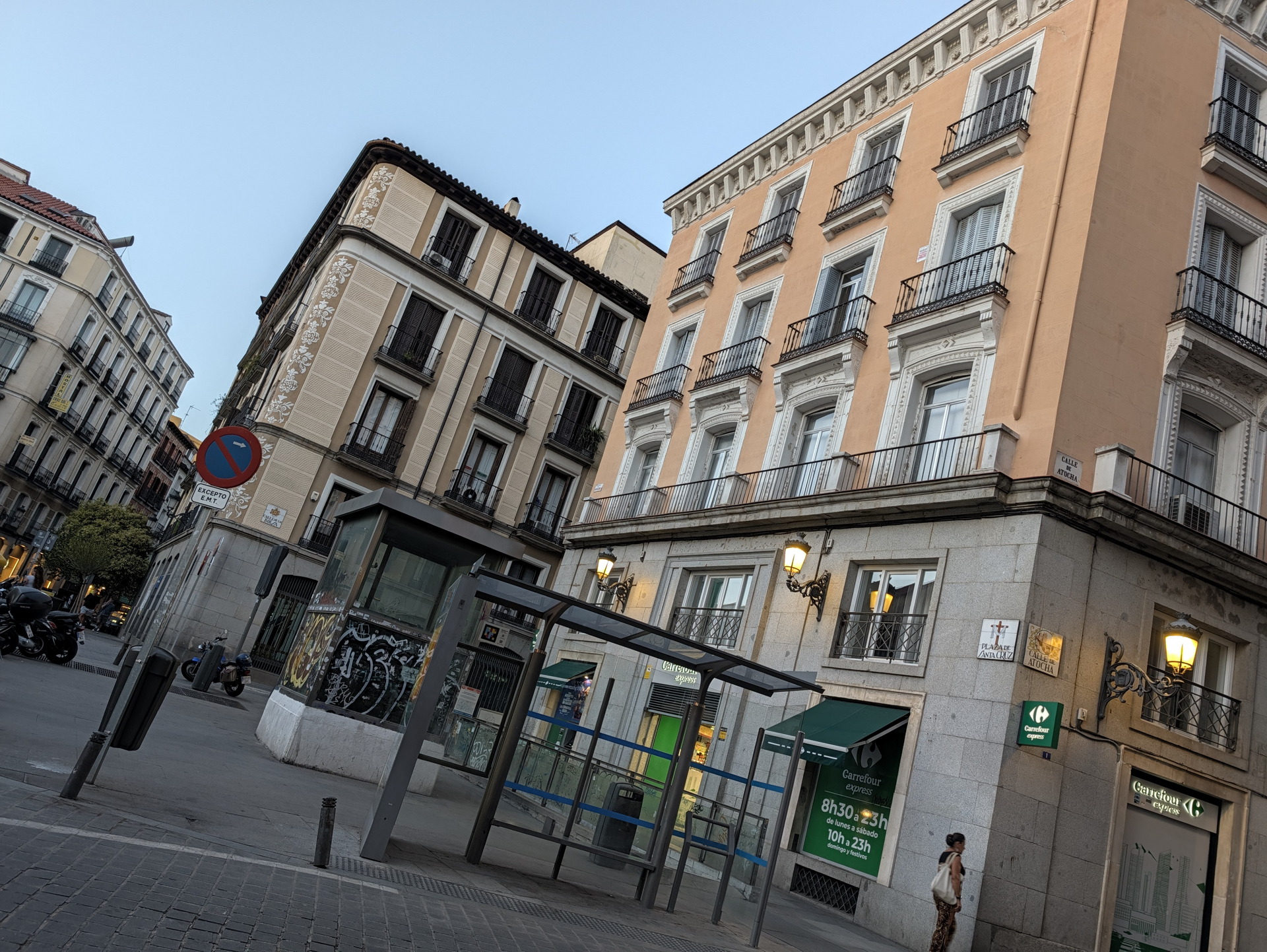 Calle con edificios históricos y supermercado en Madrid, España, con cielo despejado al atardecer.
