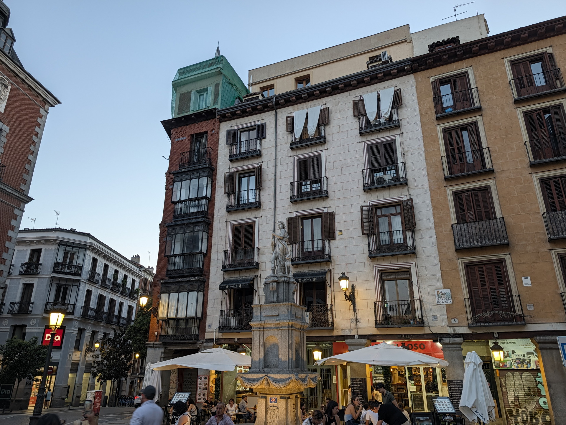 Fachadas históricas y plaza con restaurante en Madrid al atardecer, ambiente urbano y relajado.