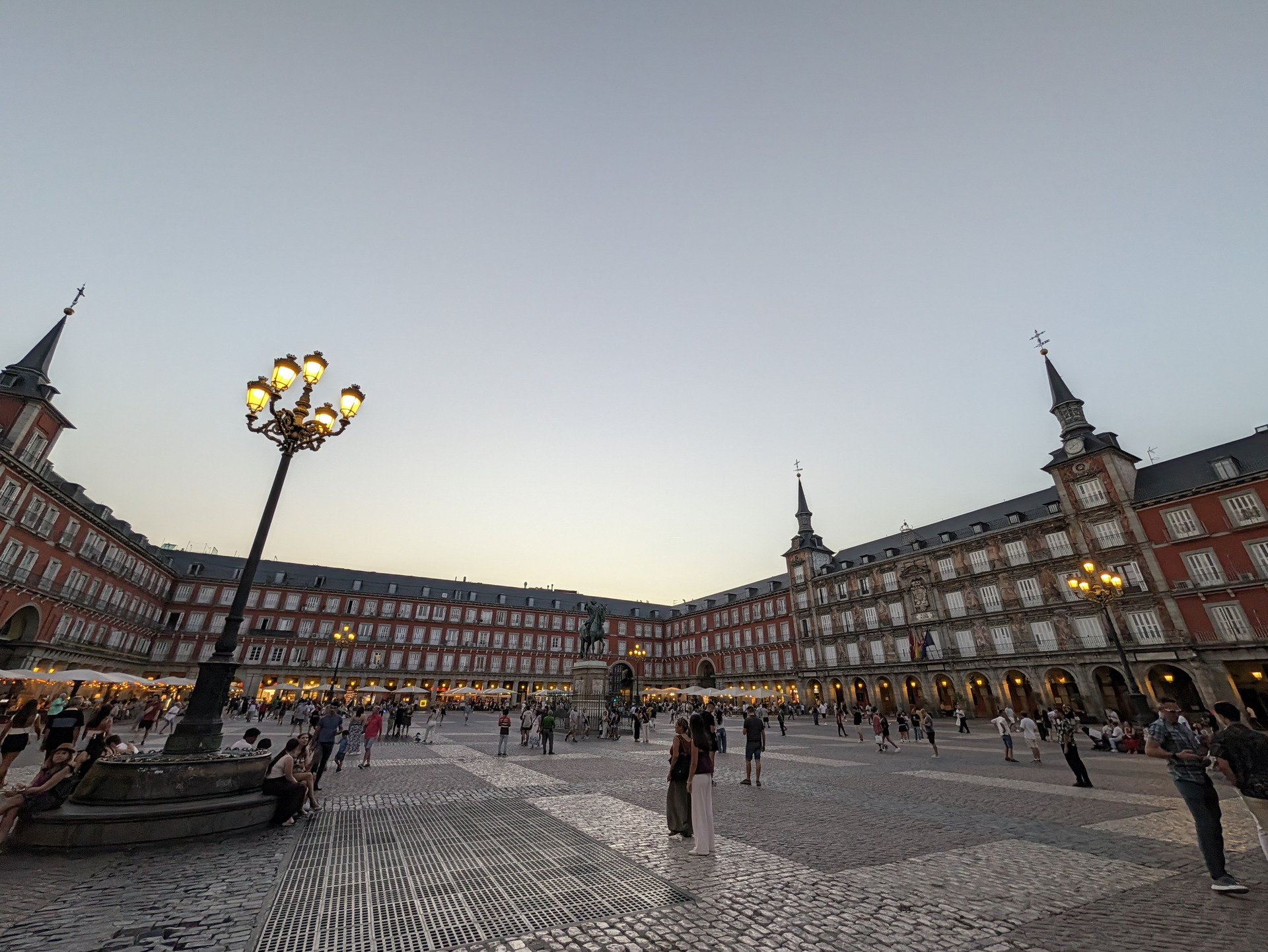 Plaza Mayor de Madrid al atardecer, con farolas encendidas y personas disfrutando del ambiente histórico y cultural.
