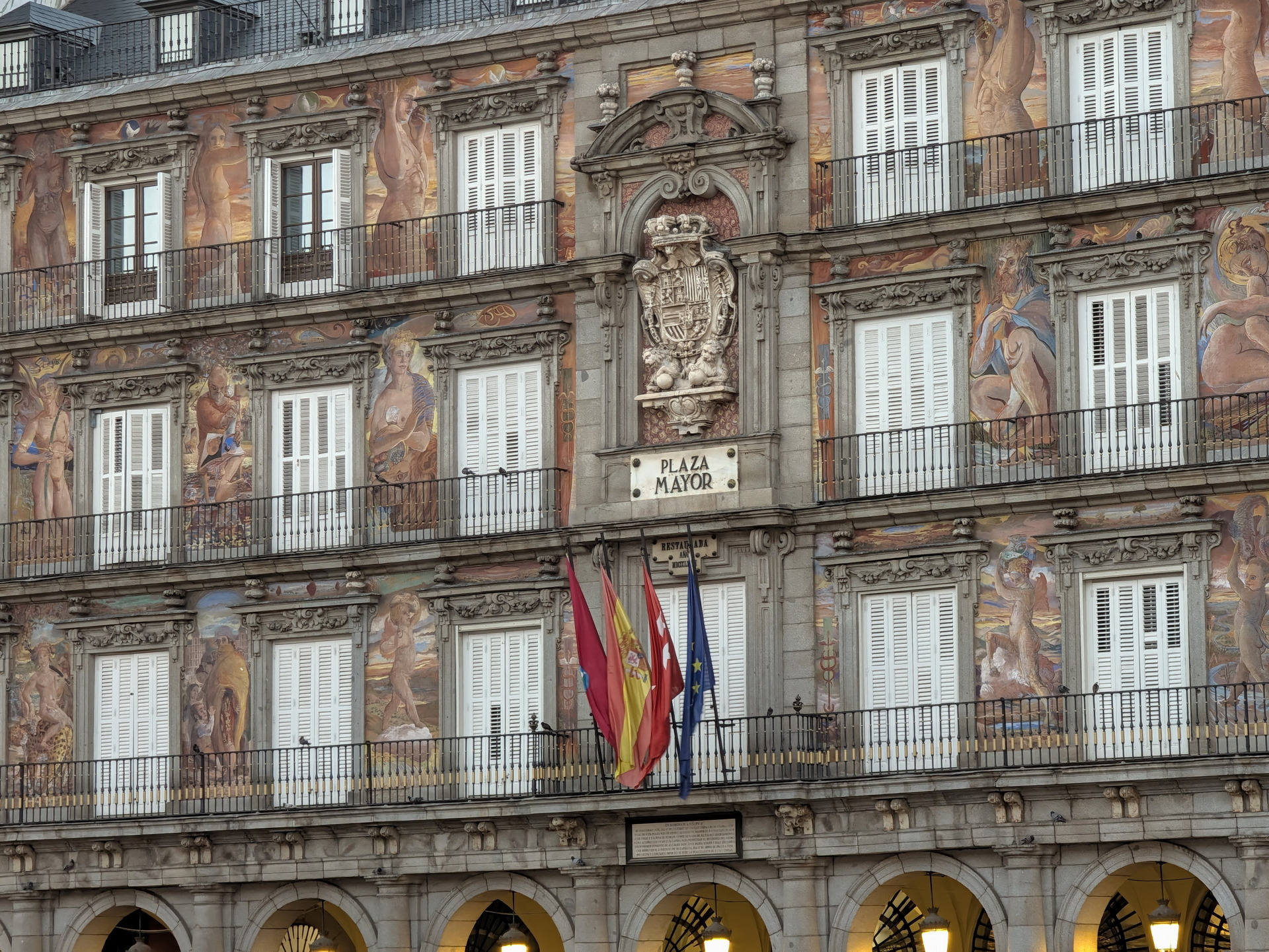 Edificio histórico en la Plaza Mayor de Madrid con balcones y murales artísticos, junto a banderas.