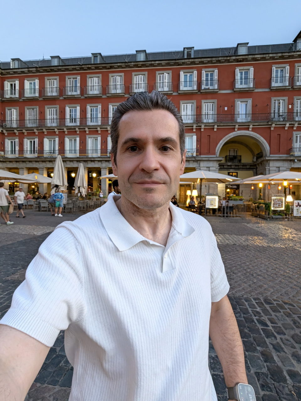 Hombre con camisa blanca en la Plaza Mayor de Madrid al atardecer, frente a un edificio histórico iluminado.
