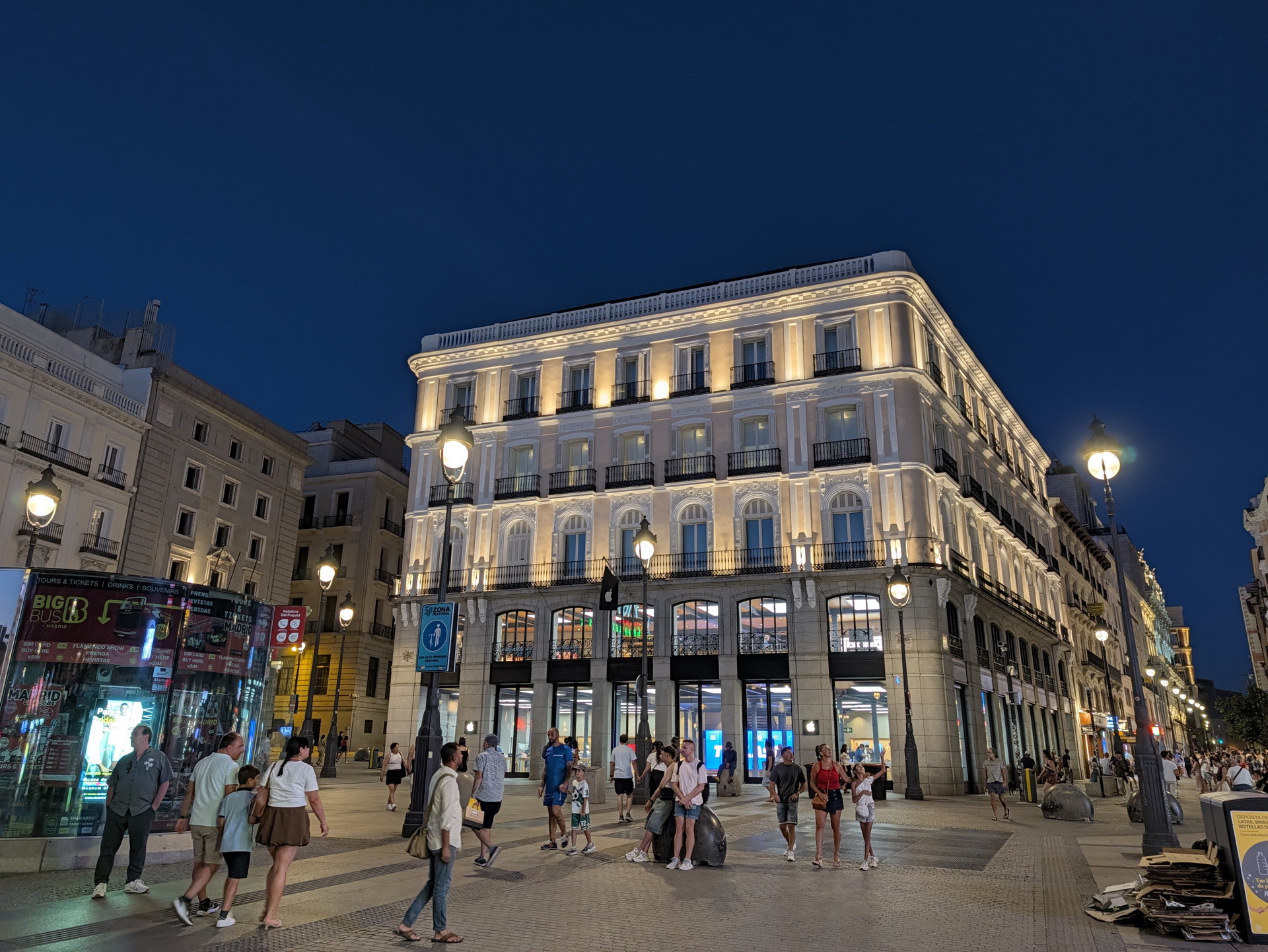 Personas pasean en plaza iluminada de noche frente a edificio histórico en Madrid.