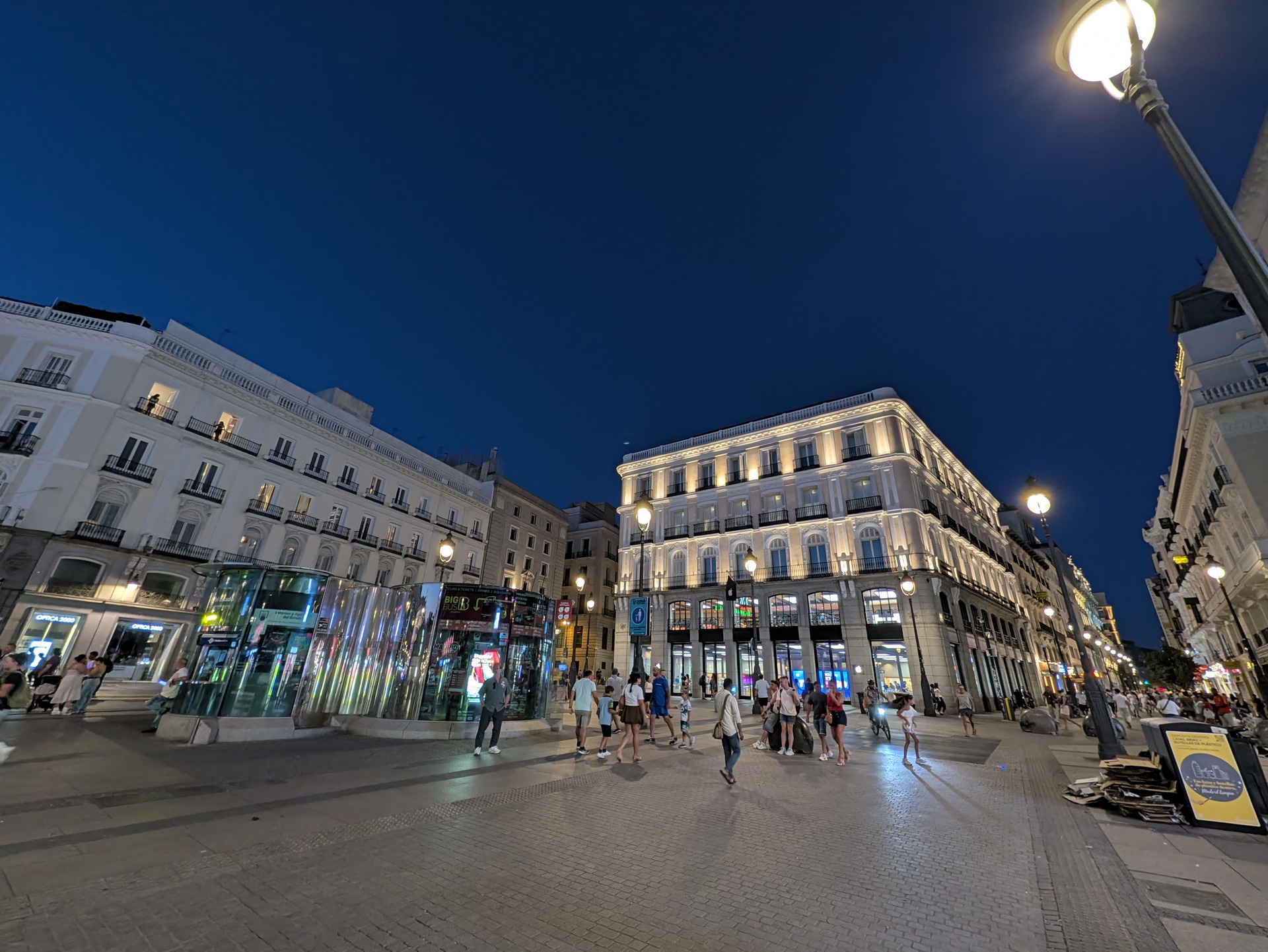 Calle iluminada de noche en Madrid con edificios y gente paseando, ambiente urbano vibrante.