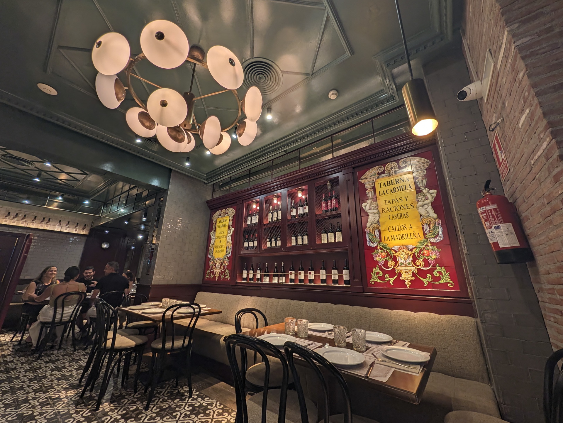 Interior de una taberna española con mesa preparada, decoración clásica y botellas de vino en estantes iluminados.
