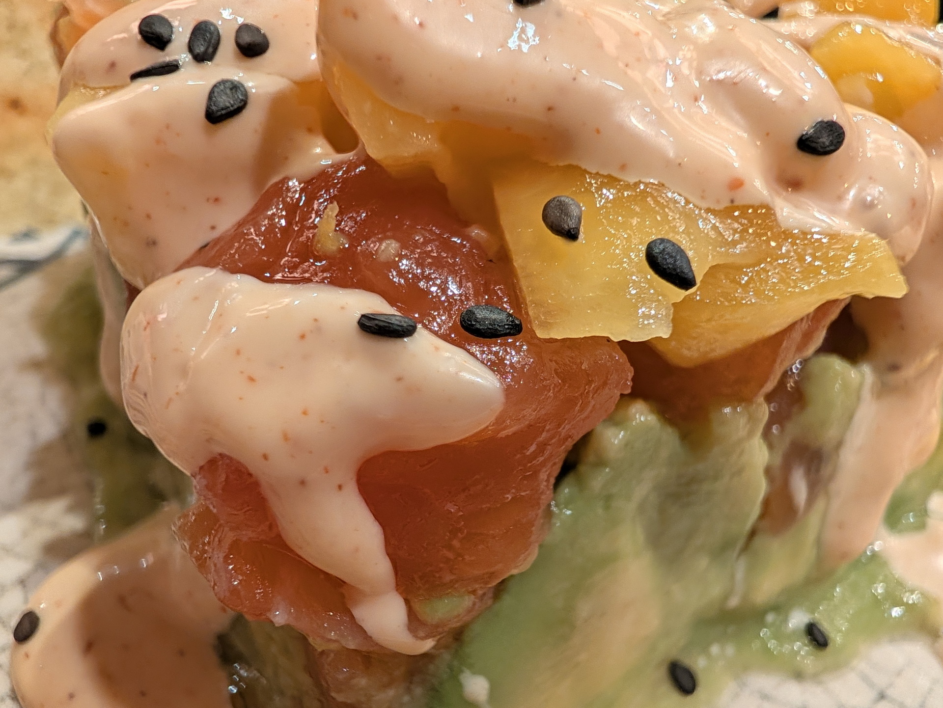Tartar de salmón con mango, aguacate y salsa cremosa, decorado con semillas de sésamo negro. Comida deliciosa.