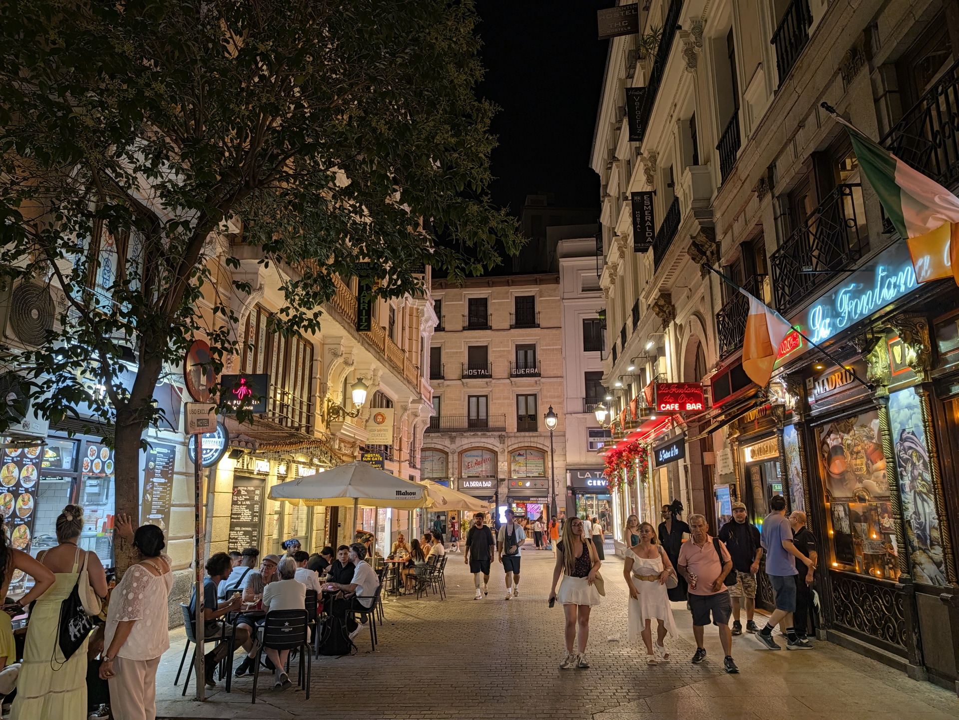 Calle iluminada de noche en Madrid con restaurantes y peatones disfrutando del ambiente urbano y luces de neón.