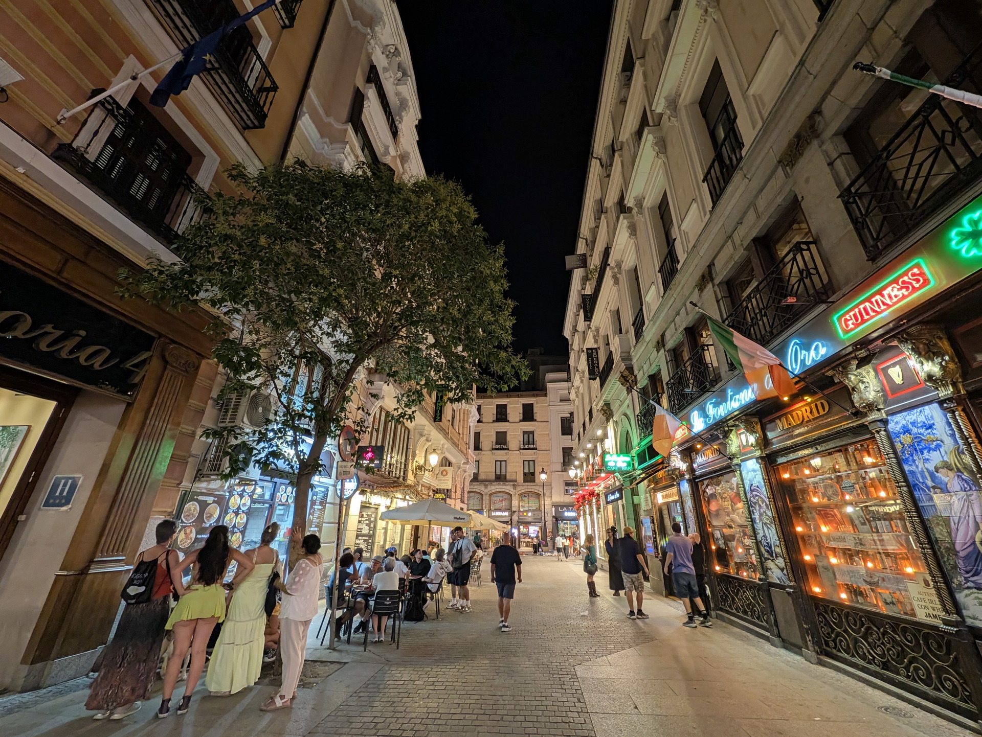 Calle animada de Madrid por la noche, con bares iluminados y personas disfrutando al aire libre.