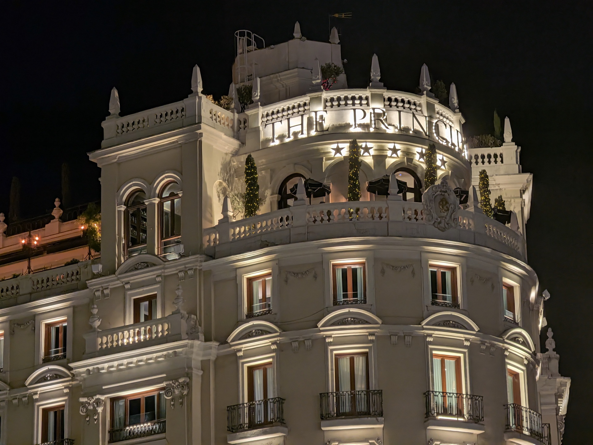 Edificio iluminado de noche con fachada clásica y ventanas adornadas en la azotea.
