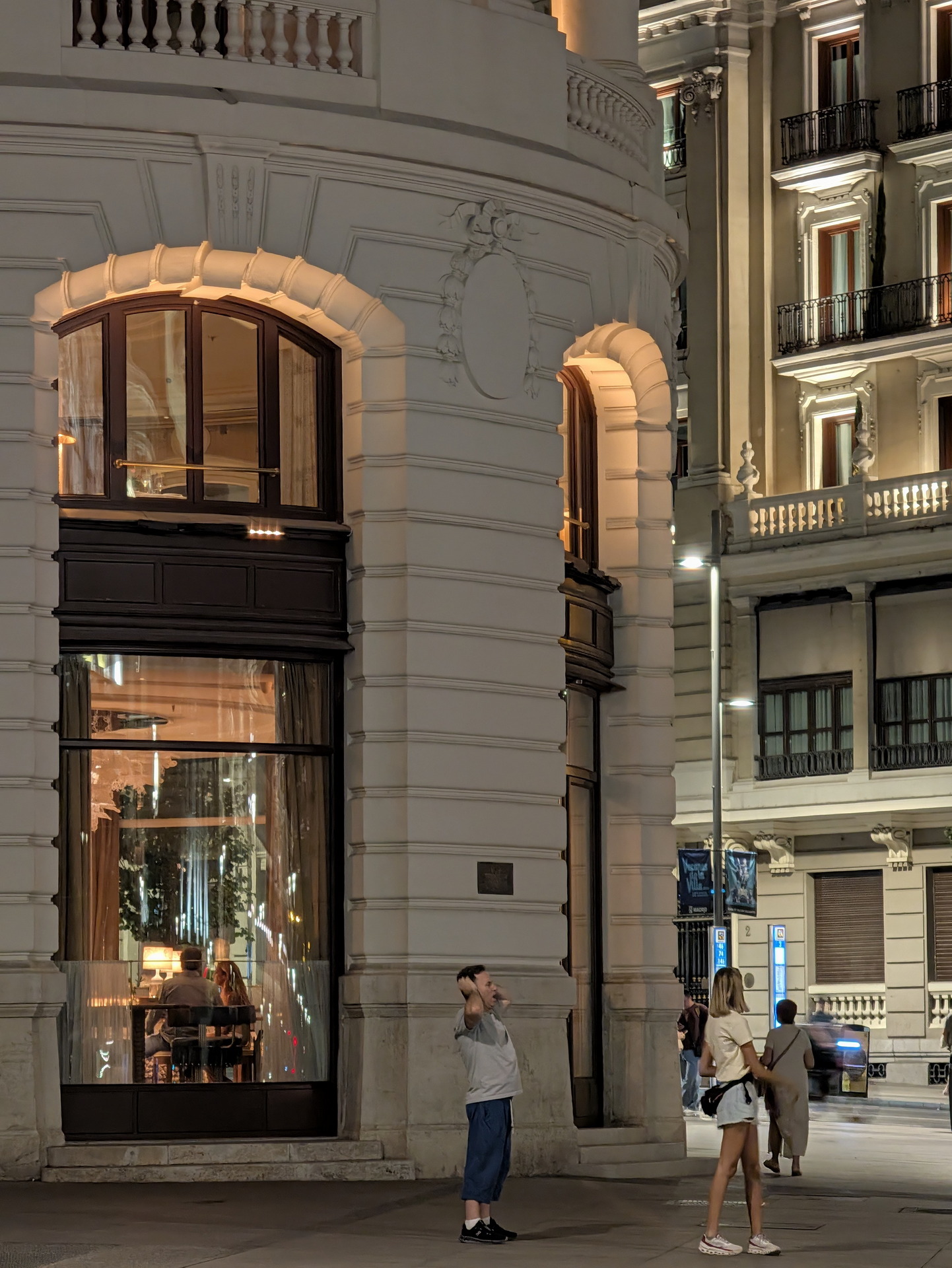 Personas de pie frente a un edificio iluminado por la noche en una calle de la ciudad.