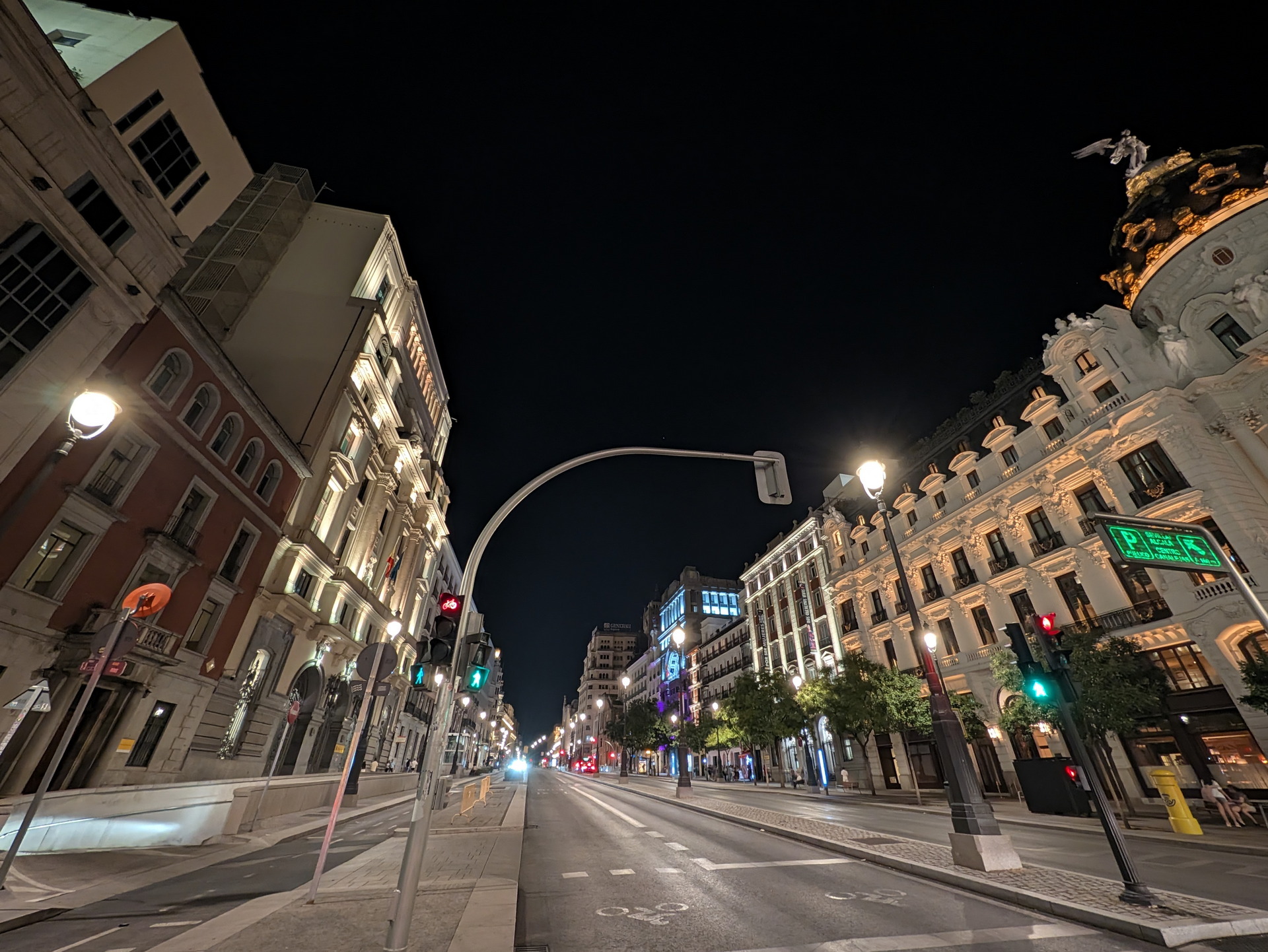 Calle Gran Vía en Madrid iluminada de noche, edificios históricos y tráfico escaso.