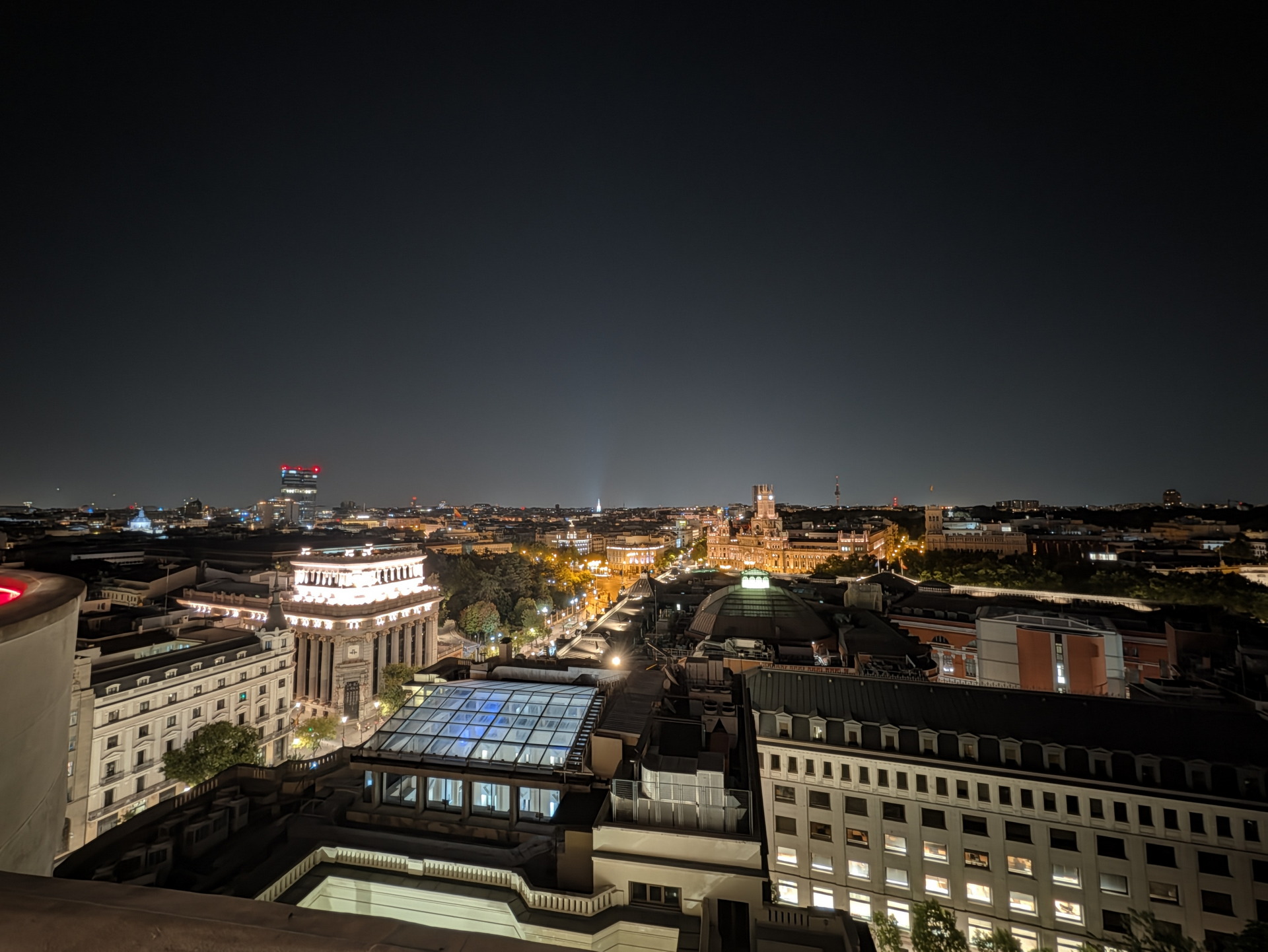 Vista nocturna aérea de una ciudad iluminada, con edificios históricos y calles resplandecientes, cielo oscuro.