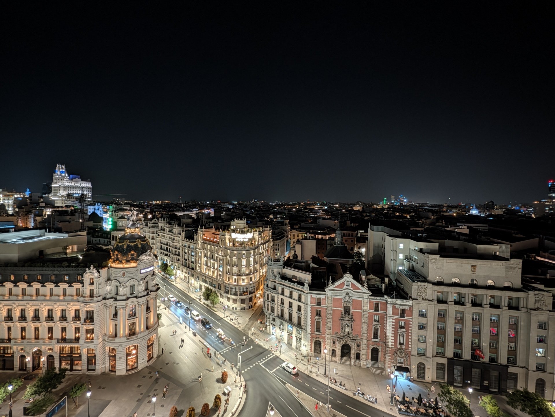 Vista nocturna de Gran Vía en Madrid iluminada, destacando edificios emblemáticos y el bullicio urbano.