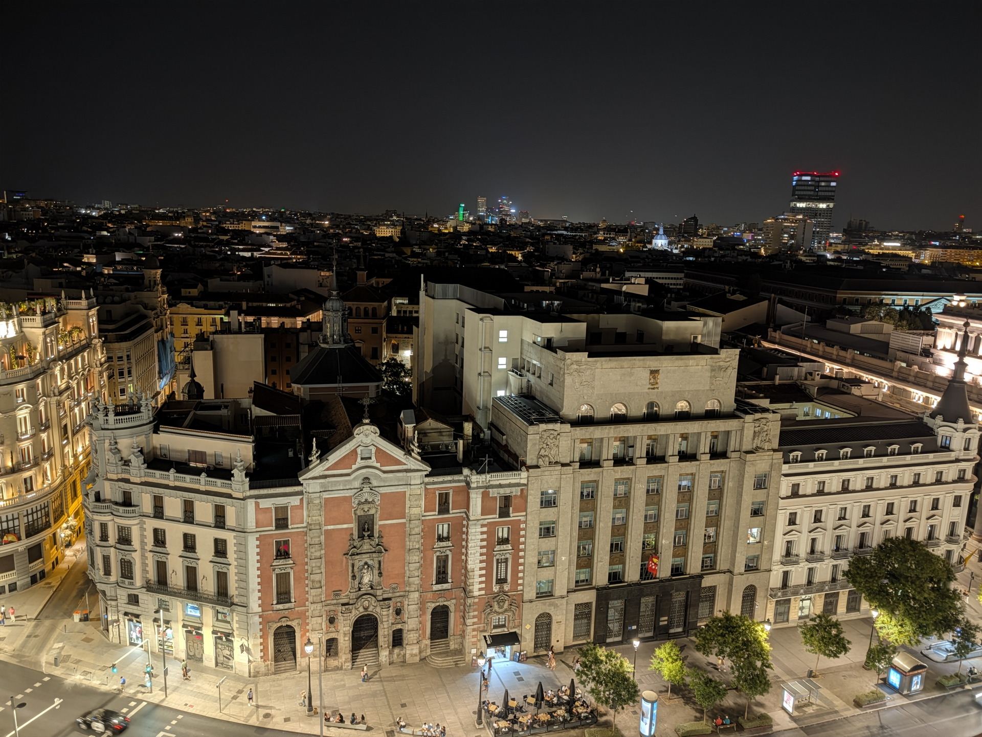 Vista nocturna de un edificio histórico en Madrid, iluminado y rodeado de calles tranquilas y casas antiguas.