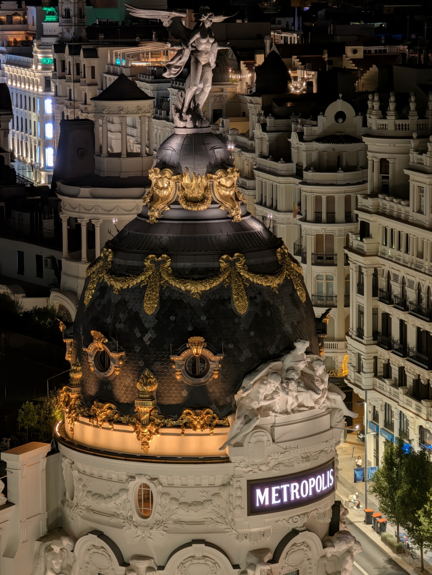 Cupula iluminada del edificio Metrópolis en Madrid, destacando su arquitectura icónica y detalles dorados.