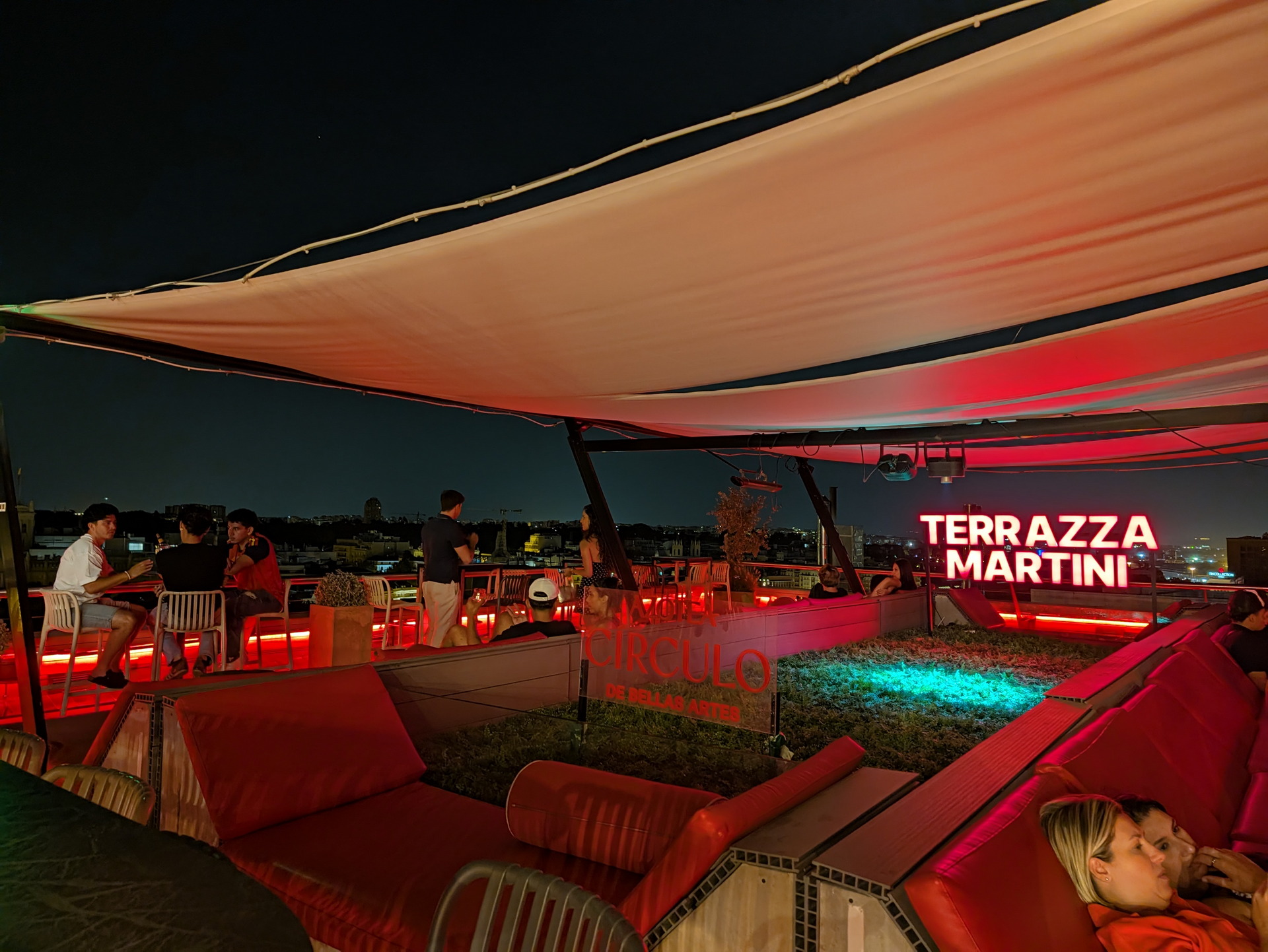 Terraza nocturna en Madrid con decoración moderna y luces rojas, vista urbana en el fondo.