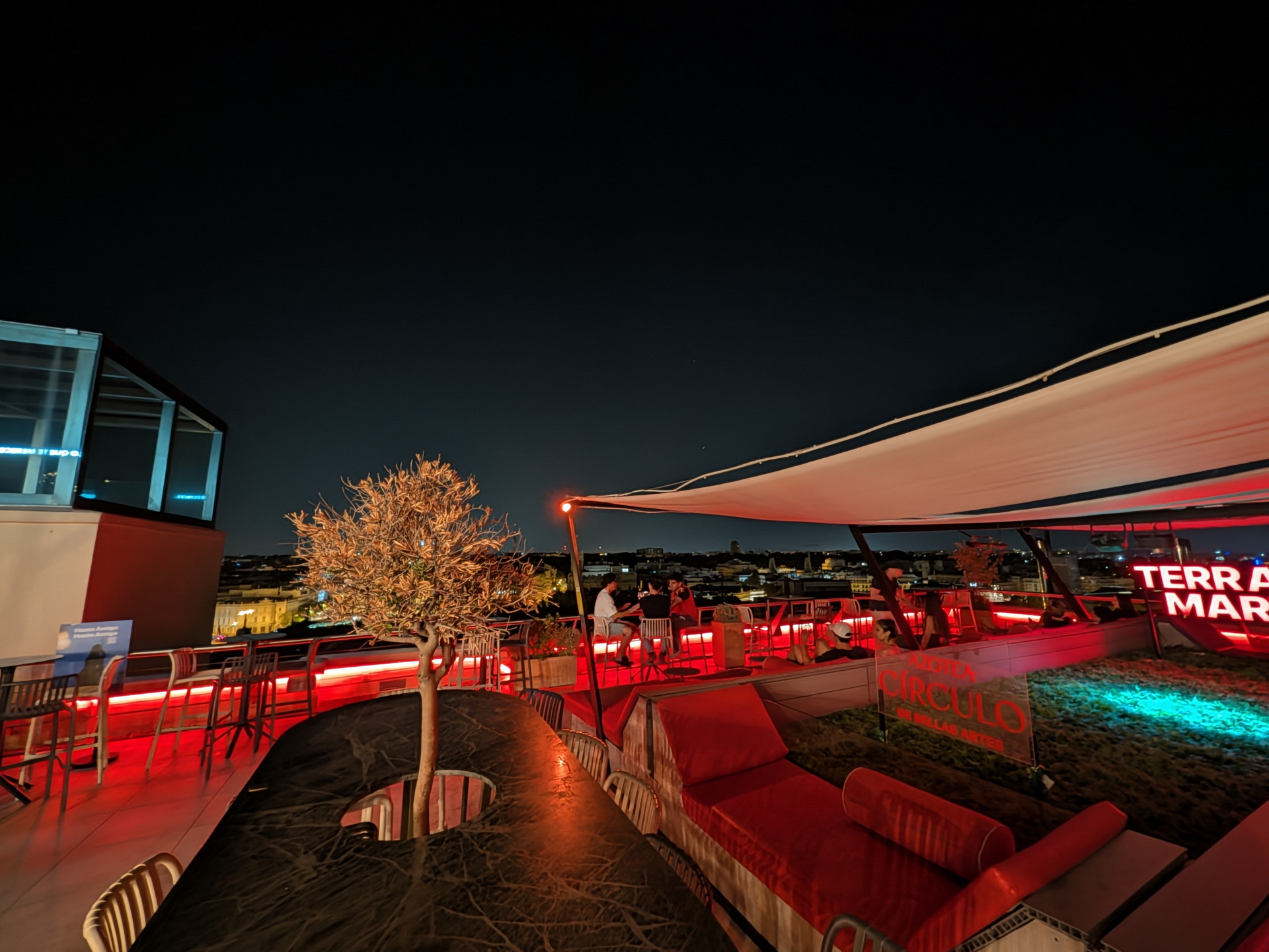 Rooftop nocturno con iluminación roja, vistas panorámicas y ambiente moderno en una terraza de la ciudad.