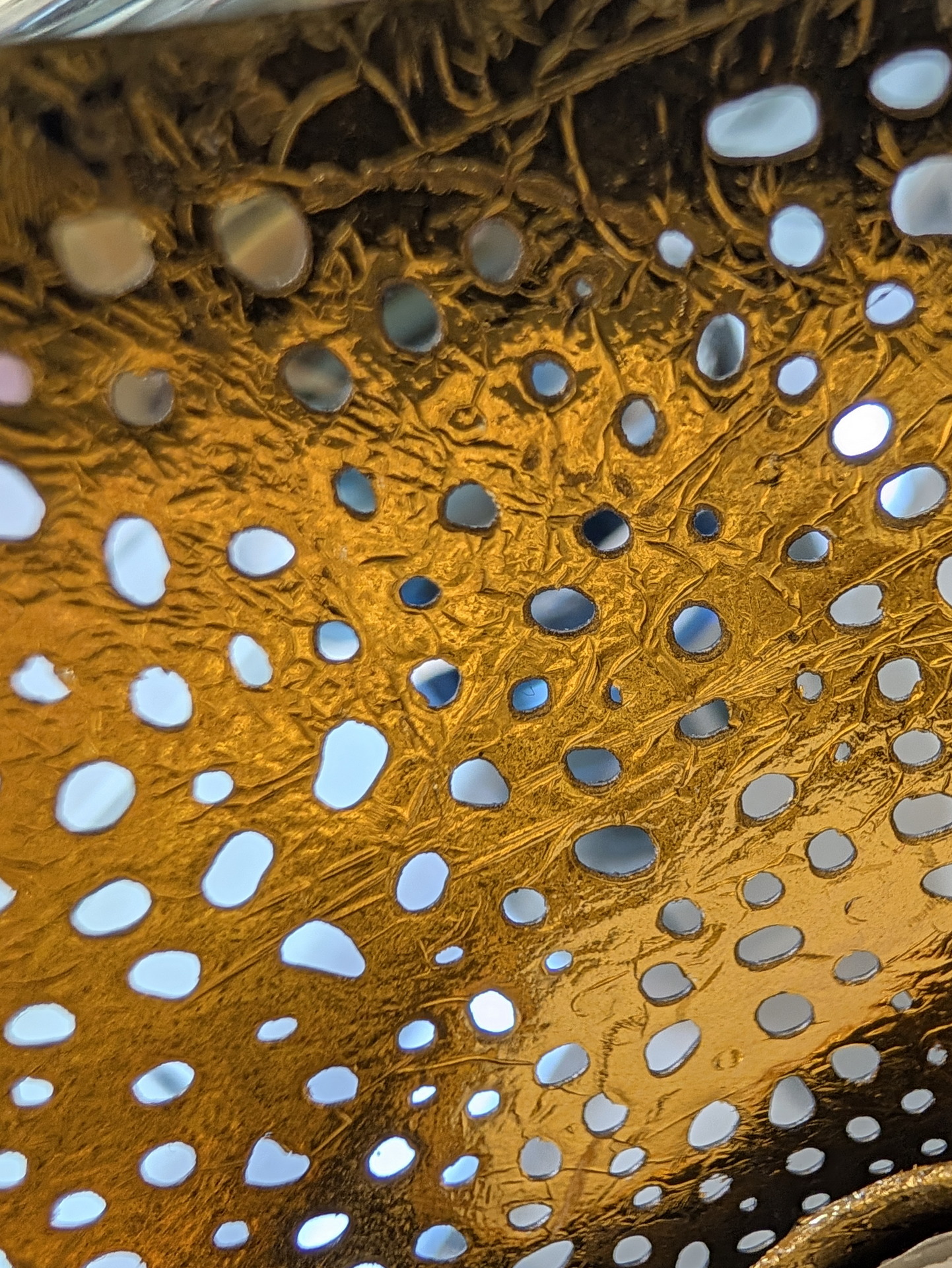 Textura metálica dorada con agujeros irregulares, vista en primer plano en un diseño abstracto y artístico.