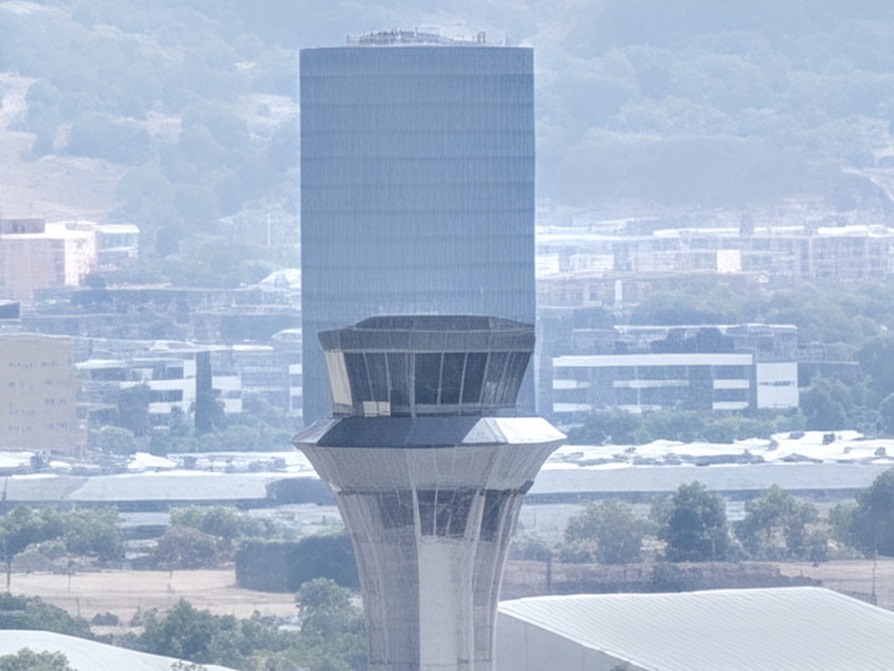 Torre de control de un aeropuerto con un moderno edificio de oficinas al fondo en un día despejado.