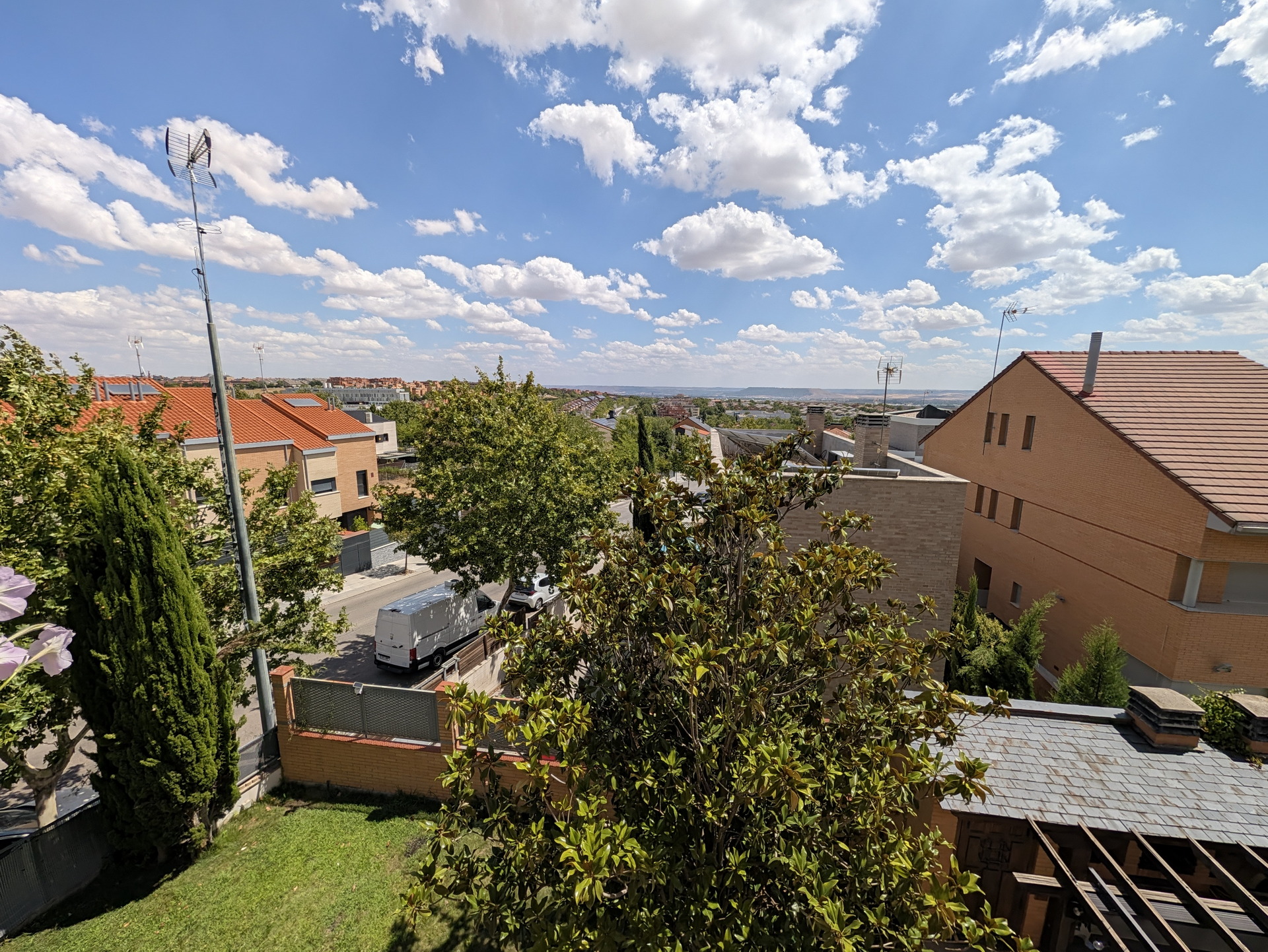 Vista panorámica de un vecindario con casas de tejados rojos y cielo azul con nubes esponjosas.