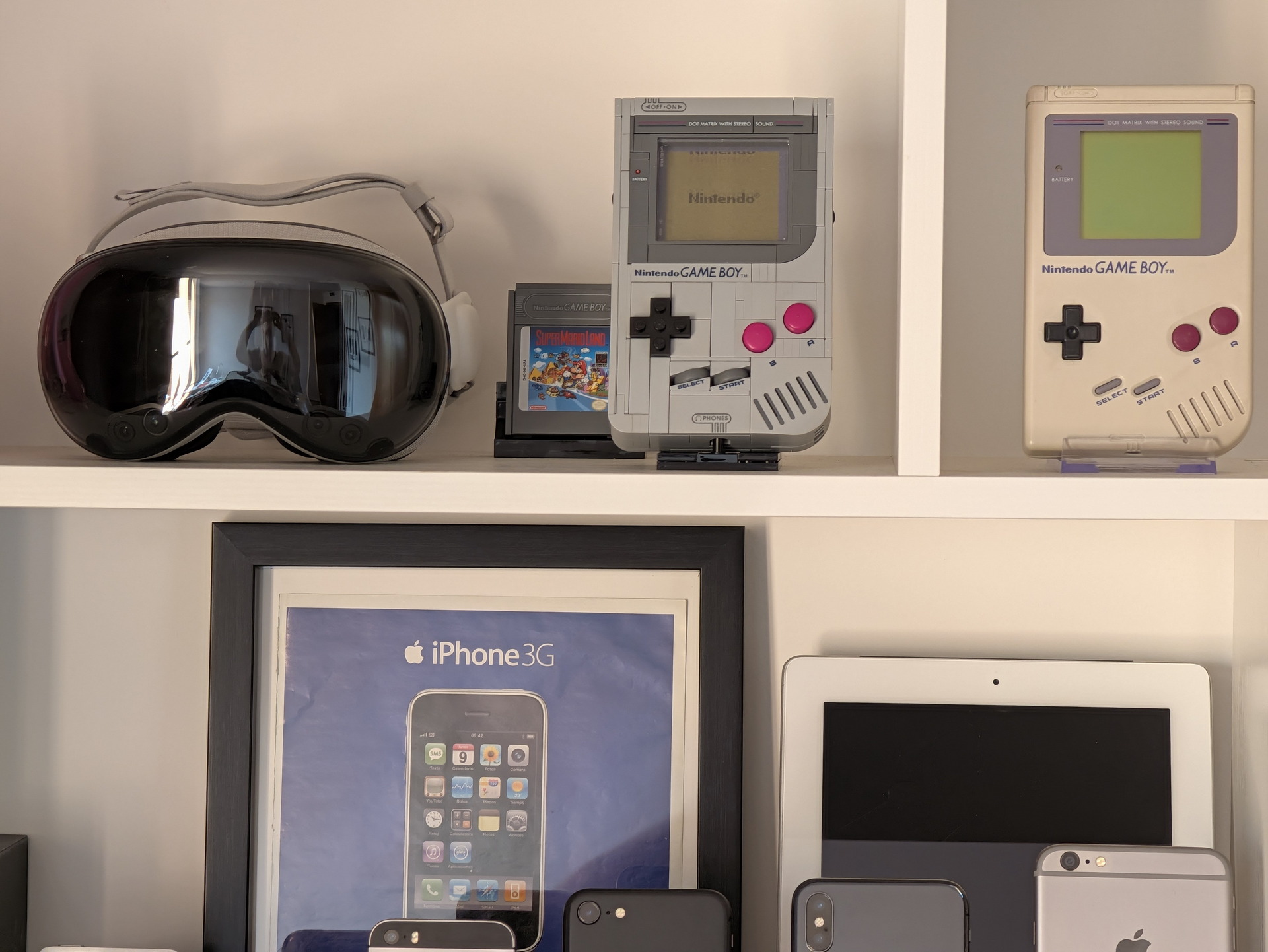 Estantes con consolas Game Boy, gafas VR y productos Apple como iPhone y iPad, resaltando tecnología retro y moderna.