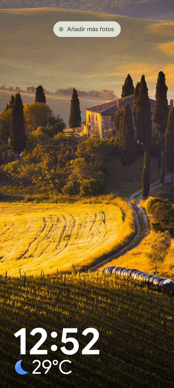 Paisaje toscano al atardecer con campo de trigo, árboles y casa rural. Hora: 12:52, temperatura: 29°C.