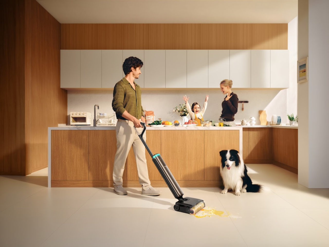 Hombre limpiando cocina moderna con aspiradora, mientras familia y perro están cerca del mostrador lleno de comida.