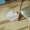 Aspiradora robot blanca limpiando el suelo de madera clara junto a una silla en una cocina moderna.