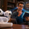 Los AirPods con cámaras de Apple revelan nuevos secretos: así podrán «ver» lo que te rodea Hombre leyendo con auriculares inteligentes y tecnología de hologramas en una sala de estar moderna.