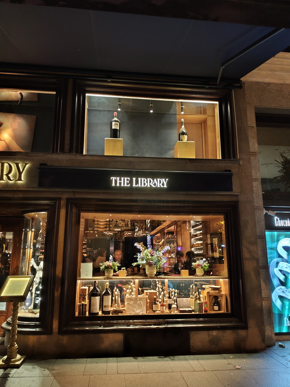 Escaparate nocturno iluminado de una tienda de vinos y decoración elegante llamado The Library.