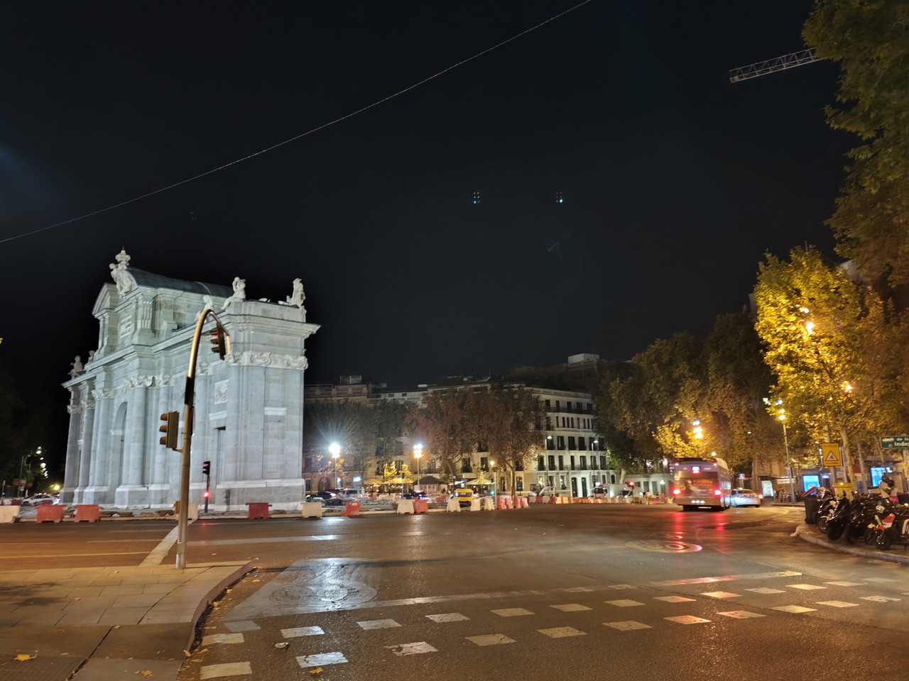 Calle iluminada de Madrid de noche con la Puerta de Alcalá y tráfico urbano alrededor.