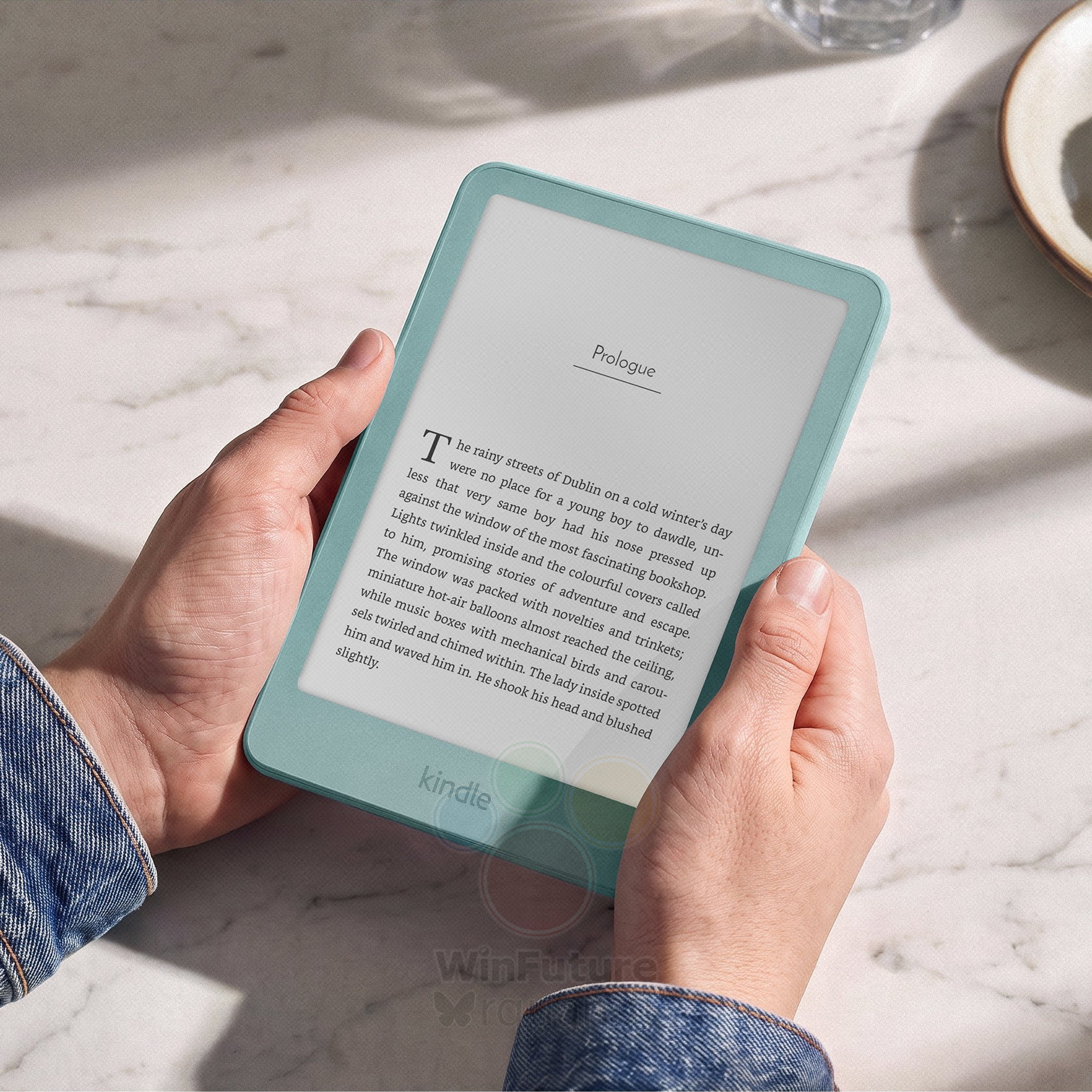 Manos sosteniendo un e-reader Kindle verde con un texto en pantalla sobre una mesa de mármol.